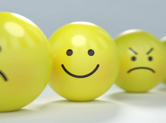 a picture of 4 yellow balls with emotive faces. the first pouting, the second is smiling, the third is angry, the last looks worried. Only the smiling face is in focus.